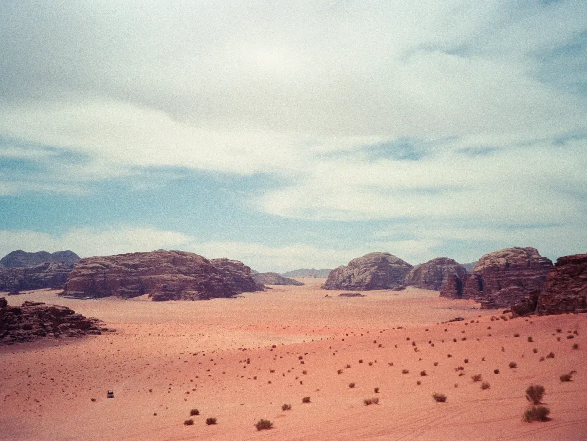 A wide desert valley with scattered scrub brush and rock outcrops under a cloudy sky.