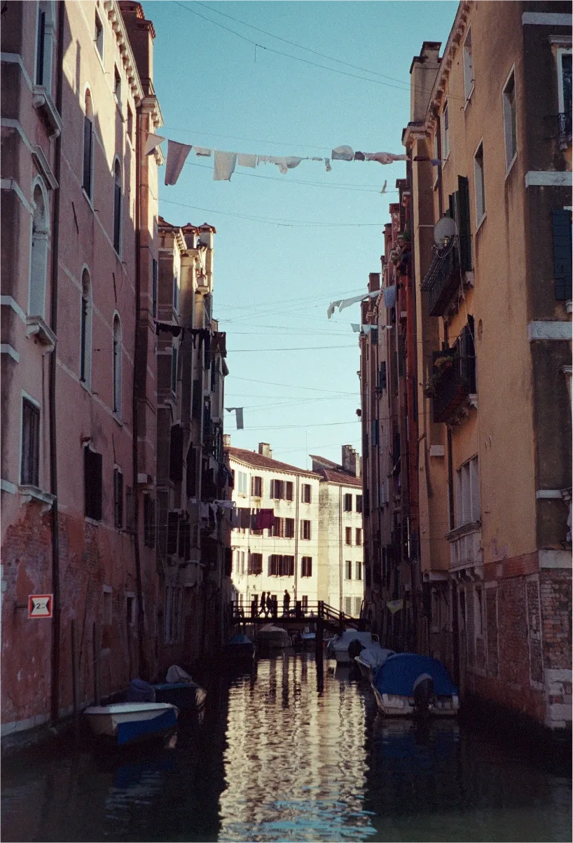 A narrow Venice canal seen between tall buildings, laundry lines strung overhead and boats moored below.