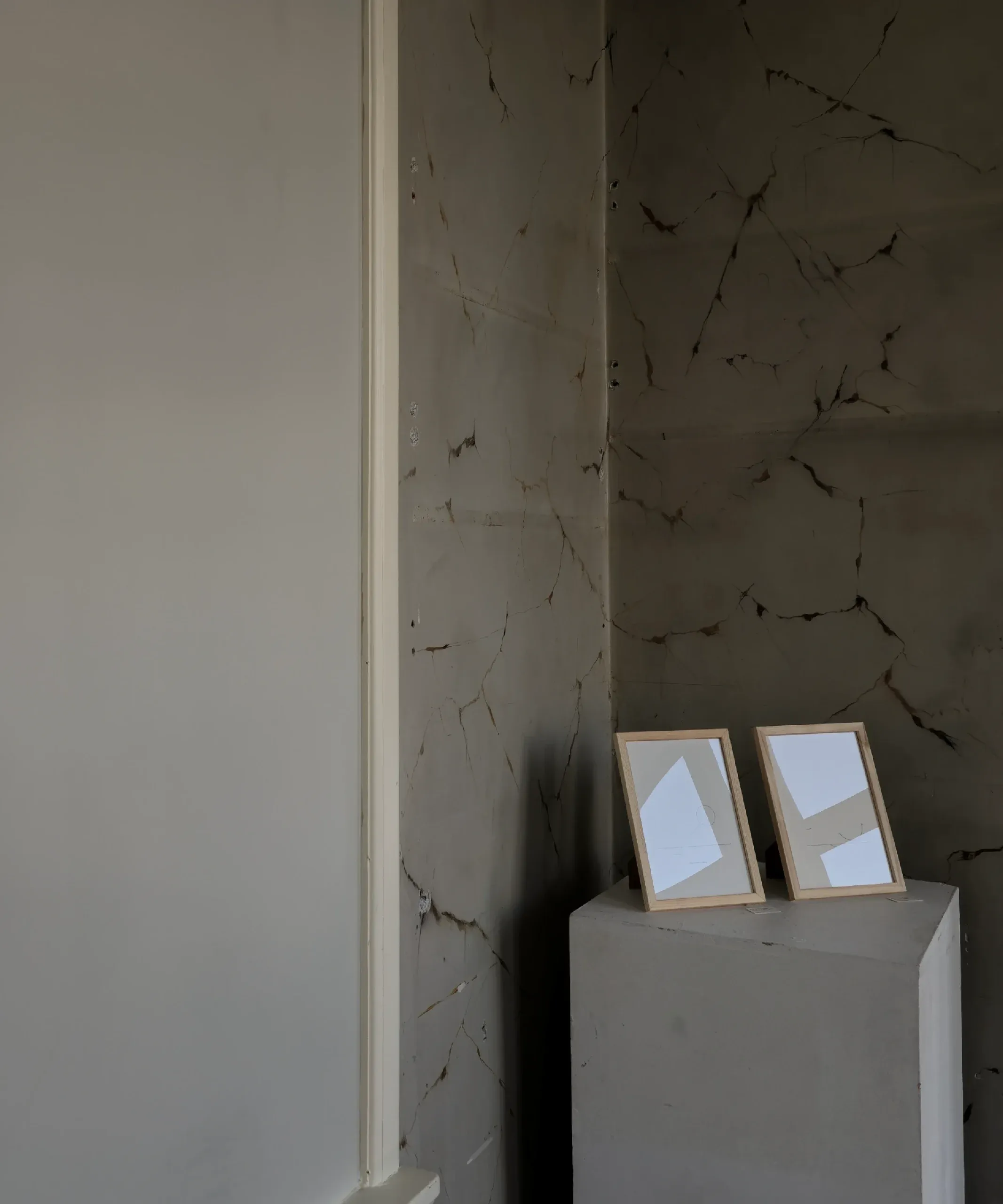 Two framed geometric drawings displayed on a pedestal against a cracked marble wall.