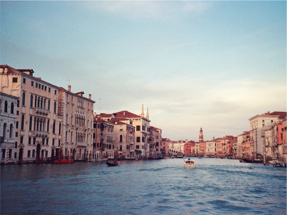 Venice's Grand Canal lined with palazzos at dusk, a boat and gondola on the water.