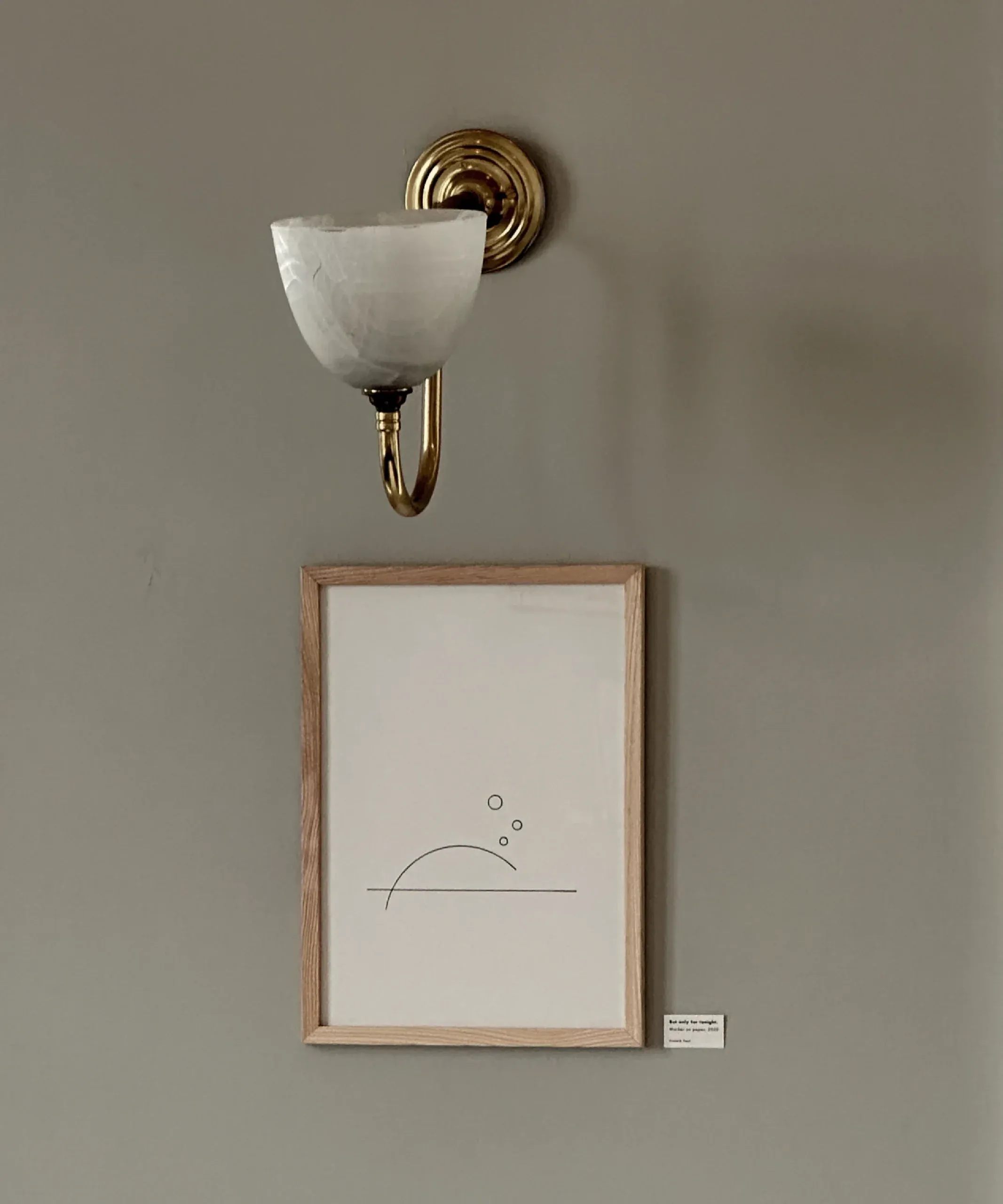 Framed line drawing 'But only for tonight,' marker on paper, lit by a brass wall sconce.