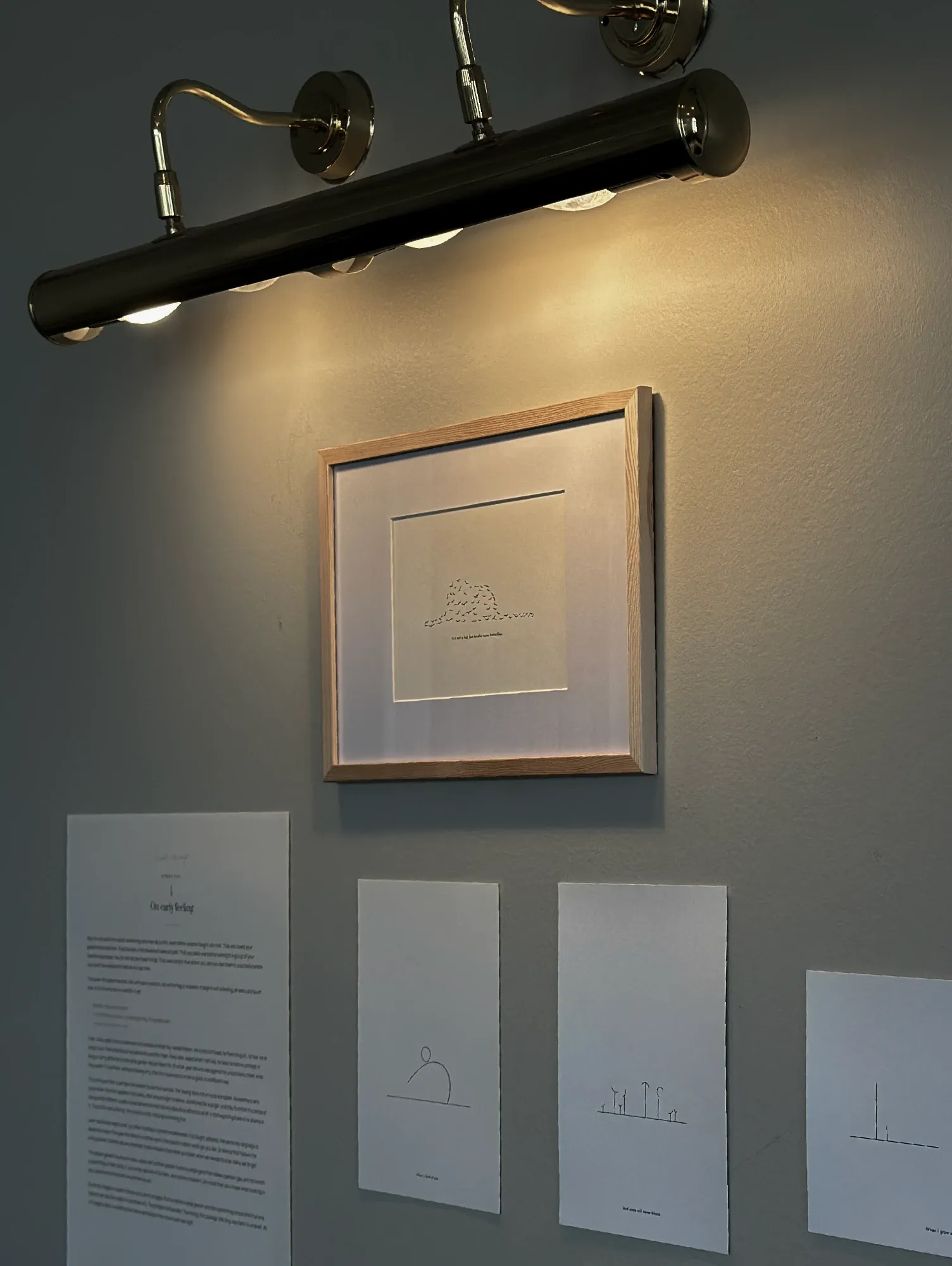 Installation view of the Quiet Courage exhibition: a framed drawing lit by a picture light, above printed story panels on the wall.